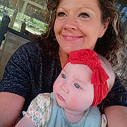 Amari is registered to the contest to win money with this photo: woman, baby, child, red_headband, curly_hair, smile, outdoor, window, reflection, greenery, portrait, holding, closeup, person, family, casual_clothing, happy, light, face, baby_clothes