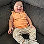 baby, child, smiling, sitting, couch, orange_top, pants, footwear, happy, face, hair, indoor, infant, cute, apparel, person, cozy, relaxed, portrait, small_child
