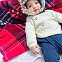 baby, child, infant, fur_hood, knitted_sweater, bear_design, plaid_blanket, red_blanket, black_blanket, blue_pants, smiling, cute, cozy, warm_clothing, portrait, indoor, lying_down, hand, face, eyes