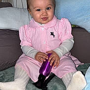 Lou participe au concours pour gagner de l'argent avec cette photo : baby, blanket, child, couch, cute, face, hands, indoor, infant, pigtails, pillows, pink_dress, portrait, purple_bottle, sitting, smiling, striped_clothing, toddler, wallpaper, white_socks