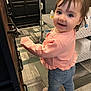 toddler, child, smiling, indoor, flooring, cabinet, clothing, jeans, pink_sweater, face, hair, person, standing, home, furniture, cart, socks, expression, happy, room