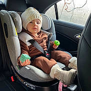 Manon a rejoint le concours — aidez-le/la à gagner de superbes lots ! baby_boots, boots, brown_outfit, car_door, car_interior, car_seat, child, child_safety, fogged_window, hat, infant, knit_hat, person, plastic_toys, seat, seatbelt, toddler, toy, window, winter_clothing