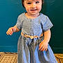 toddler, child, blue_dress, smile, standing, indoor, patterned_floor, teal_wall, short_hair, cute, person, young_child, portrait, happy, barefoot, floor_tiles, wall_texture, casual_clothing, small_person, baby