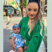 Ella participe au concours pour gagner de l'argent avec cette photo : woman, baby, child, outdoor, street, daylight, green_clothing, blue_clothing, headband, holding, portrait, people, urban, casual, fashion, sidewalk, storefront, crosswalk, person, baby_dress