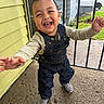 child, toddler, smiling, laughing, portrait, outdoor, porch, house, railing, overalls, denim, sneakers, autumn, leaves, happy, standing, arms_outstretched, playful, daylight, residential