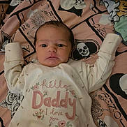 Seren is registered to the contest to win money with this photo: baby, infant, onesie, clothing, blanket, skull_pattern, skeleton_pattern, face, person, lying_down, cute, embroidery, floral_design, text_on_clothing, bedroom, indoors, newborn, expression, wide_eyes, curious