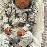 Ali is registered to the contest to win money with this photo: baby, casual_wear, child, comfortable, cozy, cute, dinosaur_print, gray_clothing, hat, hoodie, indoors, infant, knit_hat, looking_at_camera, patterned_seat, portrait, sitting, socks, toddler, young_child