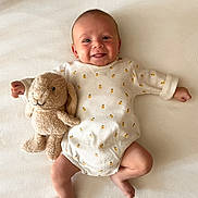Paul participe au concours pour gagner de l'argent avec cette photo : baby, smiling, infant, stuffed_animal, bunny, toy, onesie, pattern, bee, blanket, lying_down, cute, happy, child, face, skin, soft, indoor, portrait, playful