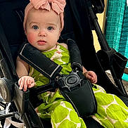 Mia joined the competition — help win amazing prizes! baby, child, stroller, headband, pink_bow, green_outfit, barefoot, infant, seatbelt, curious_look, indoor, casual_clothing, foot, face, person, cute, young_child, sitting, portrait, baby_clothes
