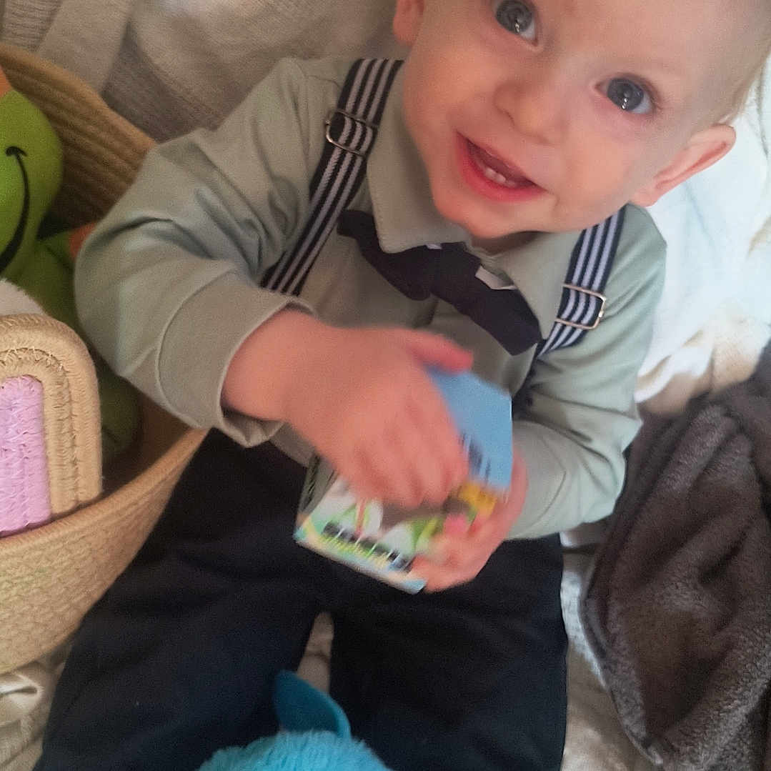 Coleson joined the competition — help win amazing prizes! basket, blanket, blue, bow_tie, child, clothing, cute, face, hand, happy, indoor, person, play, plush_toy, sitting, smile, soft, suspenders, toddler, toy