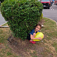 Leo joined the competition — help win amazing prizes! child, balloon, bush, greenery, grass, parking_lot, red_shoes, yellow, outdoor, nature, playful, hiding, person, casual_clothing, curly_hair, daytime, sidewalk, shrub, summer, fun