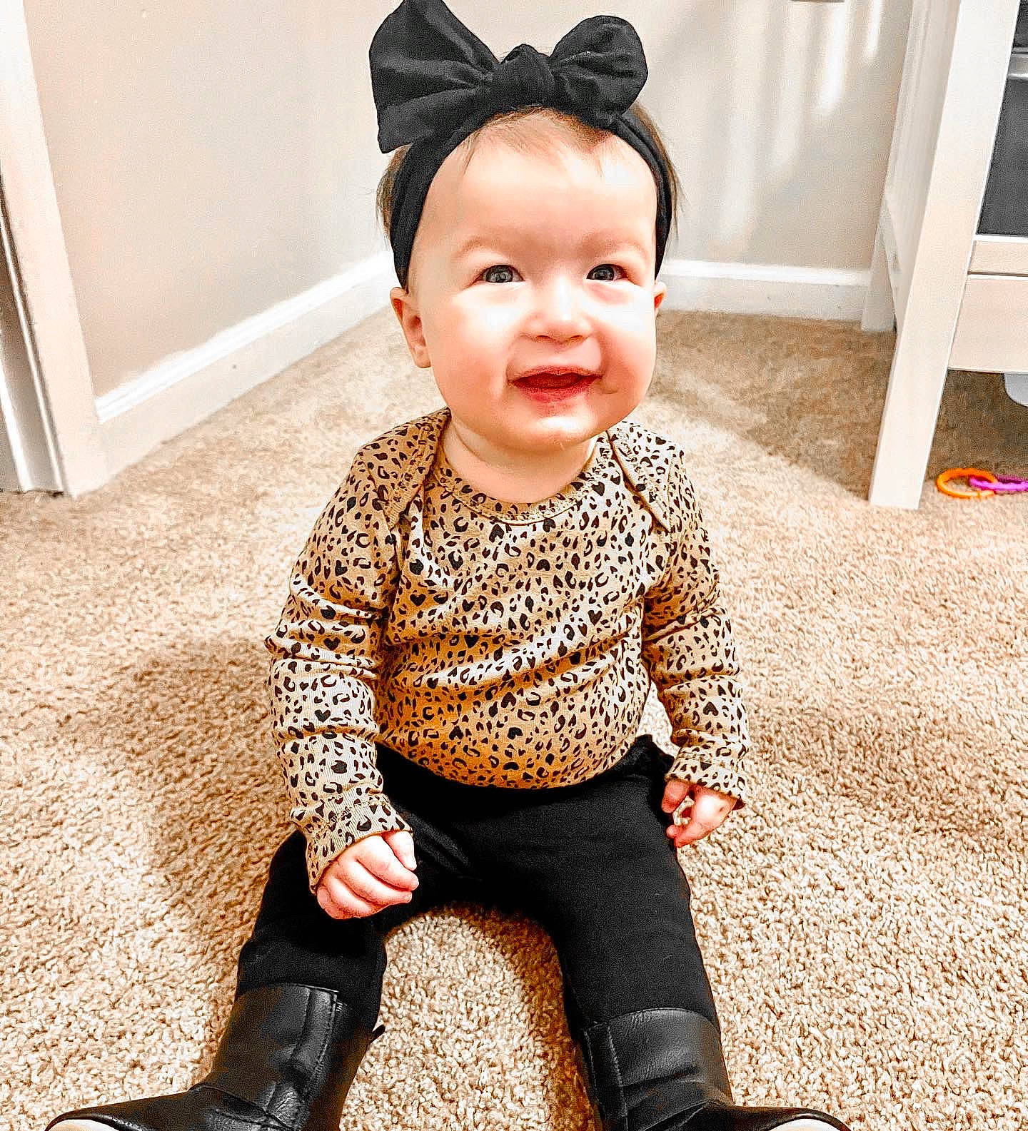 Aubriella is registered to the contest to win money with this photo: baby, baby_toddler_clothing, carmine, child, collar, face, fashion_accessory, flooring, happy, head, human_leg, knee, pattern, person, sitting, skin, sleeve, smile, t_shirt, thigh