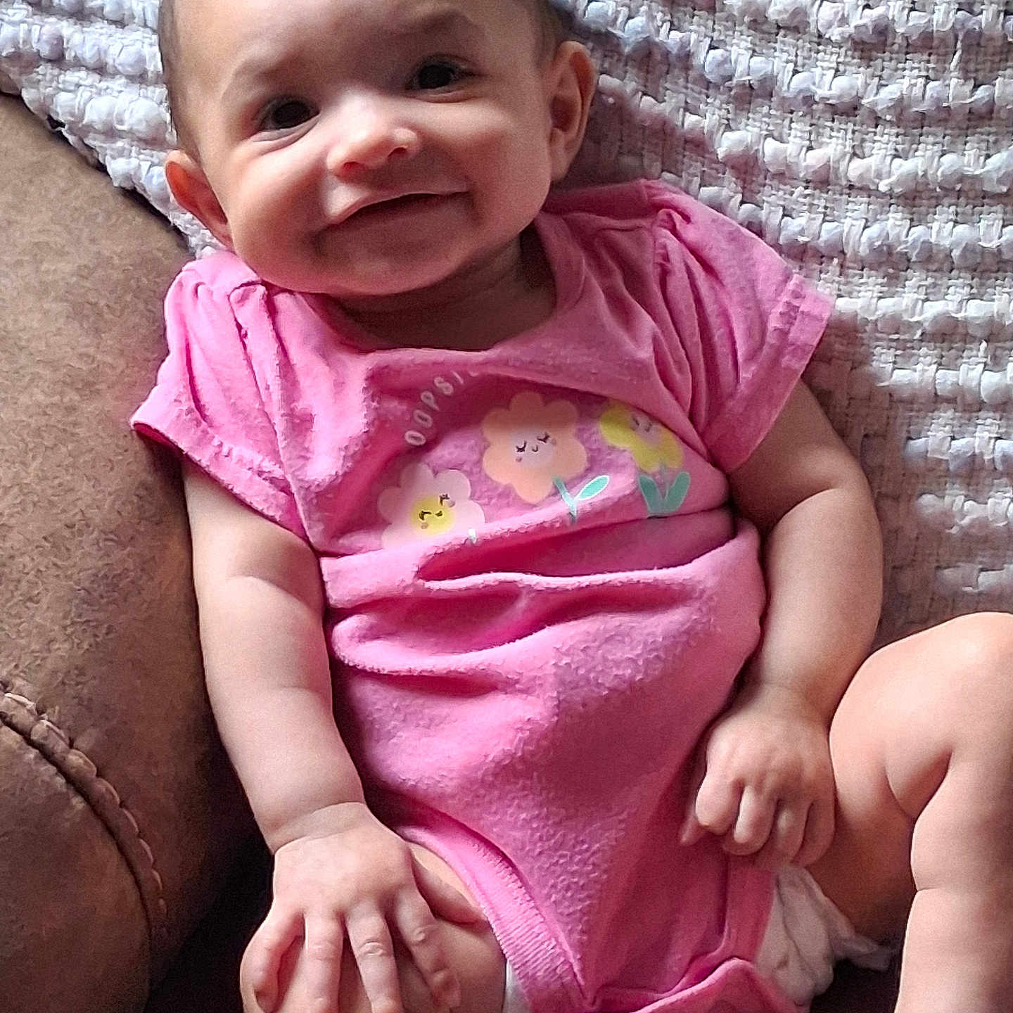 Savannah joined the competition — help win amazing prizes! baby, child, smiling, pink_onesie, flower_print, chair, leather, blanket, happy, cute, infant, portrait, sitting, hand, face, skin, comfort, indoor, young, person