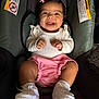 baby, smiling, infant, white_top, pink_shorts, knitted_booties, car_seat, warning_labels, happy, cute, child, indoors, portrait, young_child, clothing, seat, raised_fists, black_hair, baby_accessories, seatbelt