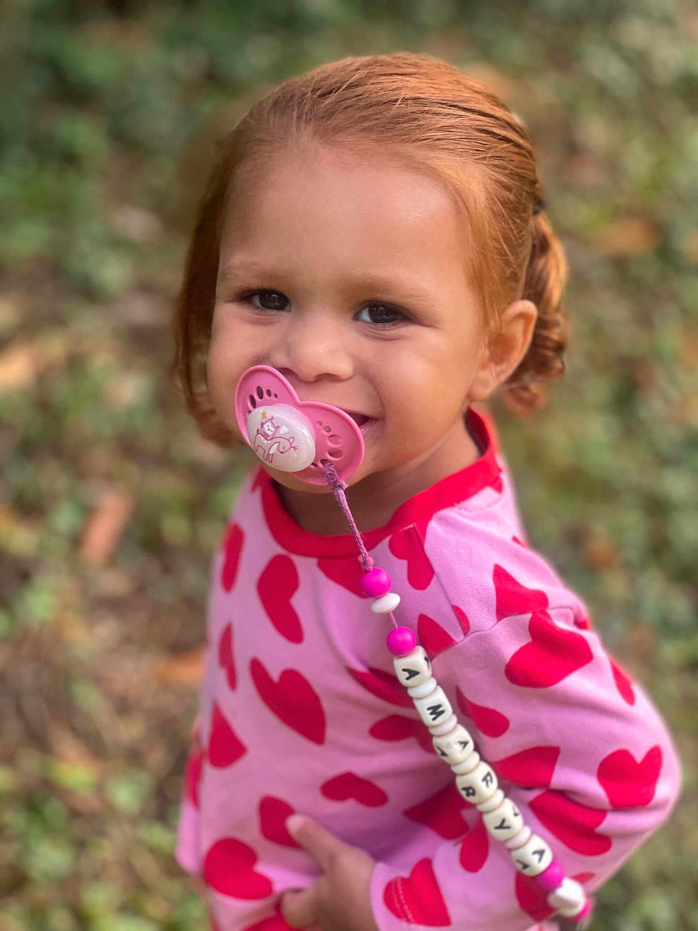 Amarya participe au concours pour gagner de l'argent avec cette photo : toddler, child, pacifier, red_hair, pink_shirt, hearts, outdoor, greenery, smiling, happy, cute, beads, clothing, person, portrait, baby, young_child, playful, nature, closeup