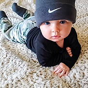 Kane is registered to the contest to win money with this photo: baby, child, beanie, hat, carpet, camo_pants, black_top, lying_down, indoors, curious, blue_eyes, cute, soft_texture, hand, face, portrait, infant, fashion, young_child, floor