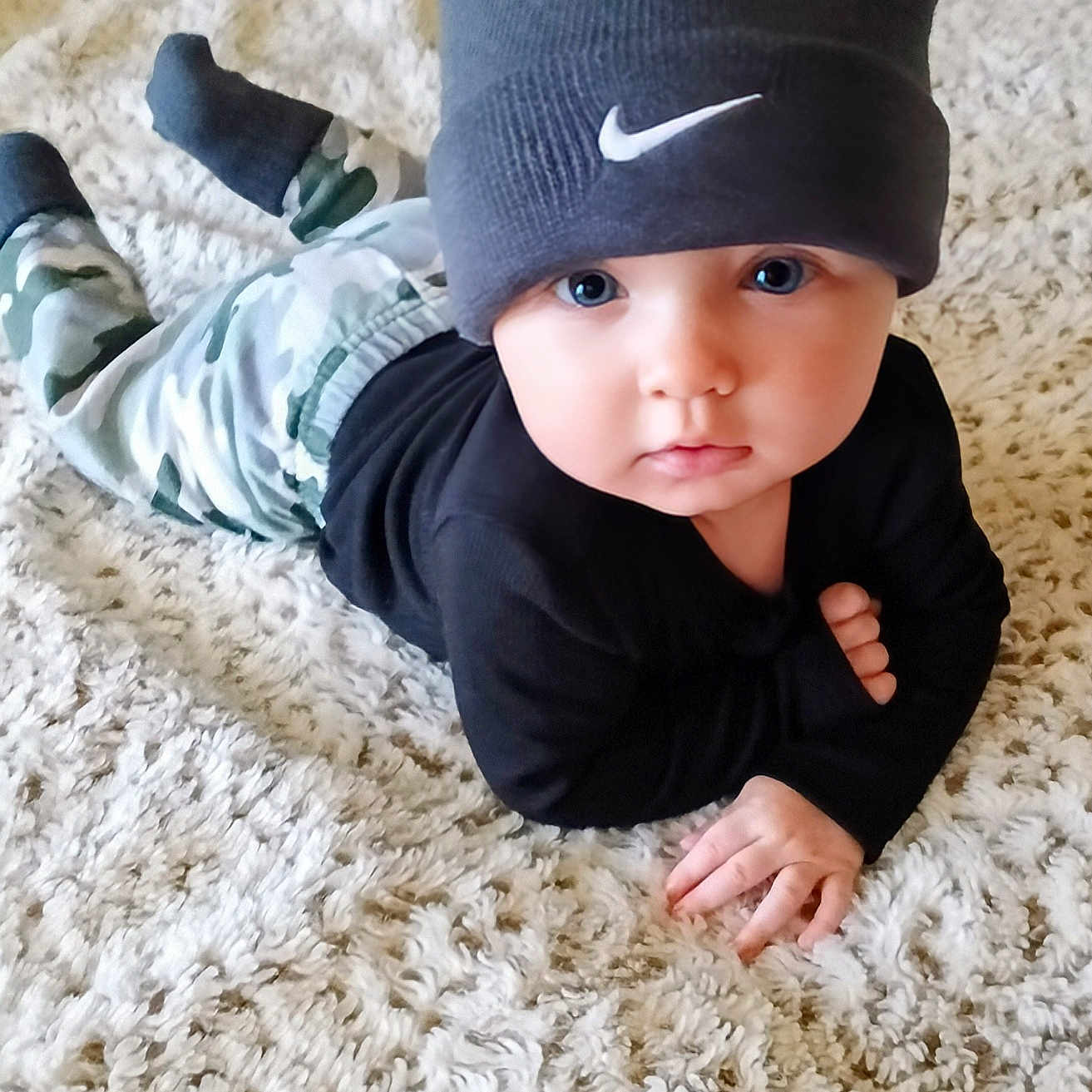 Kane is registered to the contest to win money with this photo: baby, beanie, black_top, blue_eyes, camo_pants, carpet, child, curious, cute, face, fashion, floor, hand, hat, indoors, infant, lying_down, portrait, soft_texture, young_child