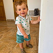 Raphaël participe au concours pour gagner de l'argent avec cette photo : toddler, child, smiling, indoor, standing, shirt, shorts, sandals, floor, door, hand, face, person, curly_hair, expression, young, home, marble_floor, wooden_door, playful