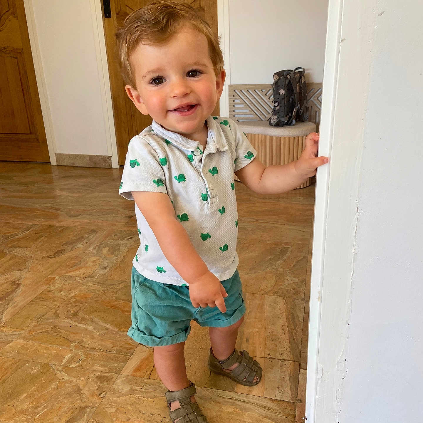 Raphaël participe au concours pour gagner de l'argent avec cette photo : child, curly_hair, door, expression, face, floor, hand, home, indoor, marble_floor, person, playful, sandals, shirt, shorts, smiling, standing, toddler, wooden_door, young