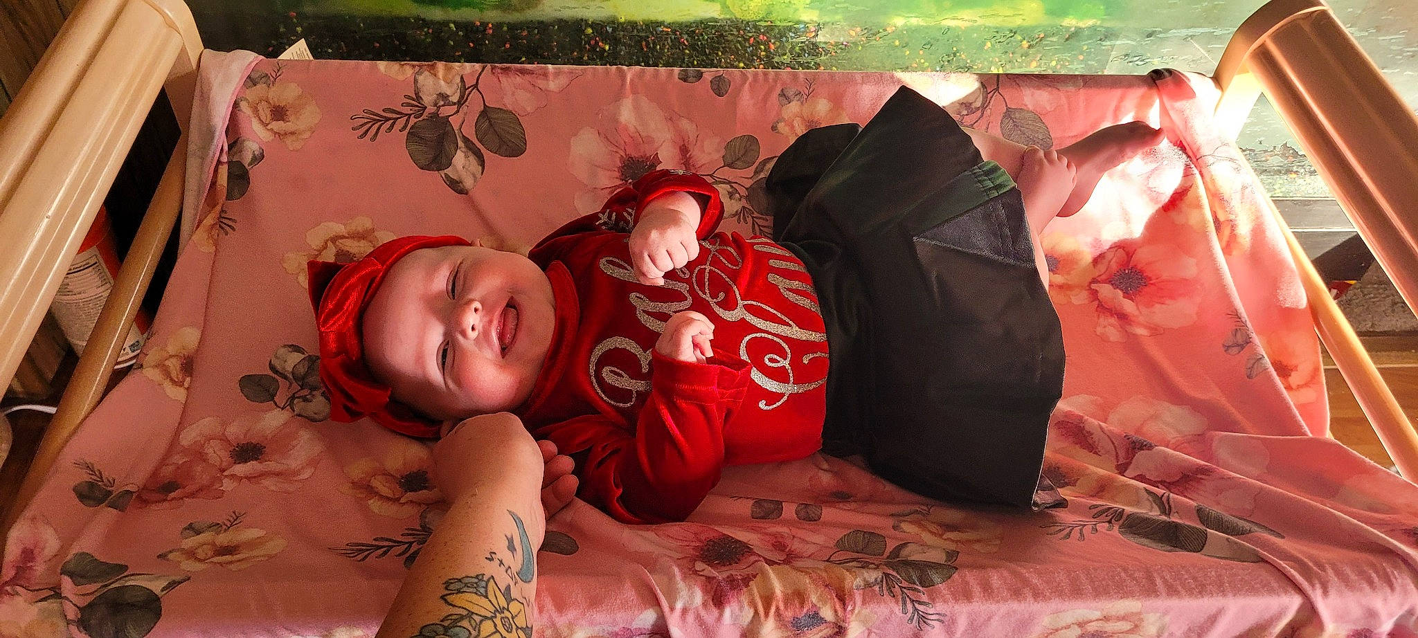 Thea is registered to the contest to win money with this photo: abdomen, arm, baby, child, comfort, flesh, flooring, grass, headwear, human_leg, linens, muscle, pattern, person, plant, sitting, smile, tattoo, toddler, tree