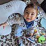 Roméo a rejoint le concours — aidez-le/la à gagner de superbes lots ! baby, bandana, child, clothing, colorful, cute, floor, happy, indoor, overalls, person, pillow, playmat, sitting, smiling, sneakers, sunlight, toddler, toys, window