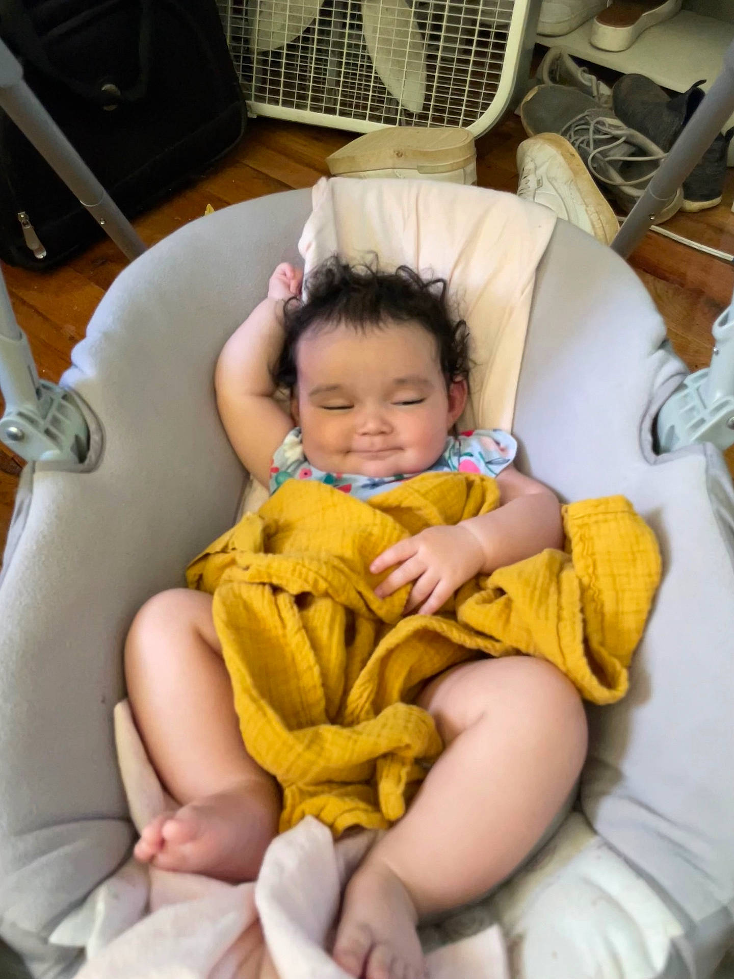 Skyla is registered to the contest to win money with this photo: baby, baby_swing, blanket, child, clothing, curly_hair, cute, fan, footwear, home, indoors, infant, person, relaxed, resting, shoes, sleepy, smile, toddler, wooden_floor