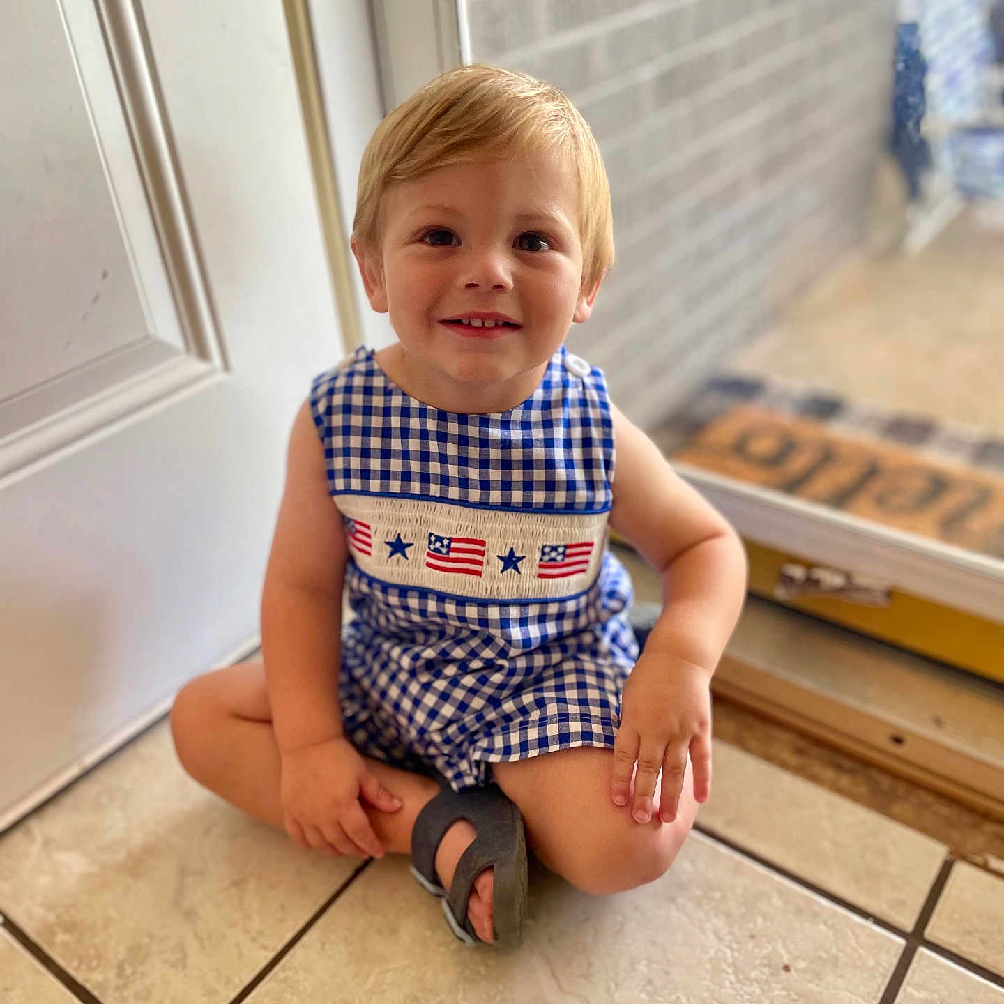 James is registered to the contest to win money with this photo: baby, bathroom, blonde, clothing, door, face, hair, happy, hardwood, head, mat, pants, person, photography, portrait, shorts, sitting, sleeve, smile, wood