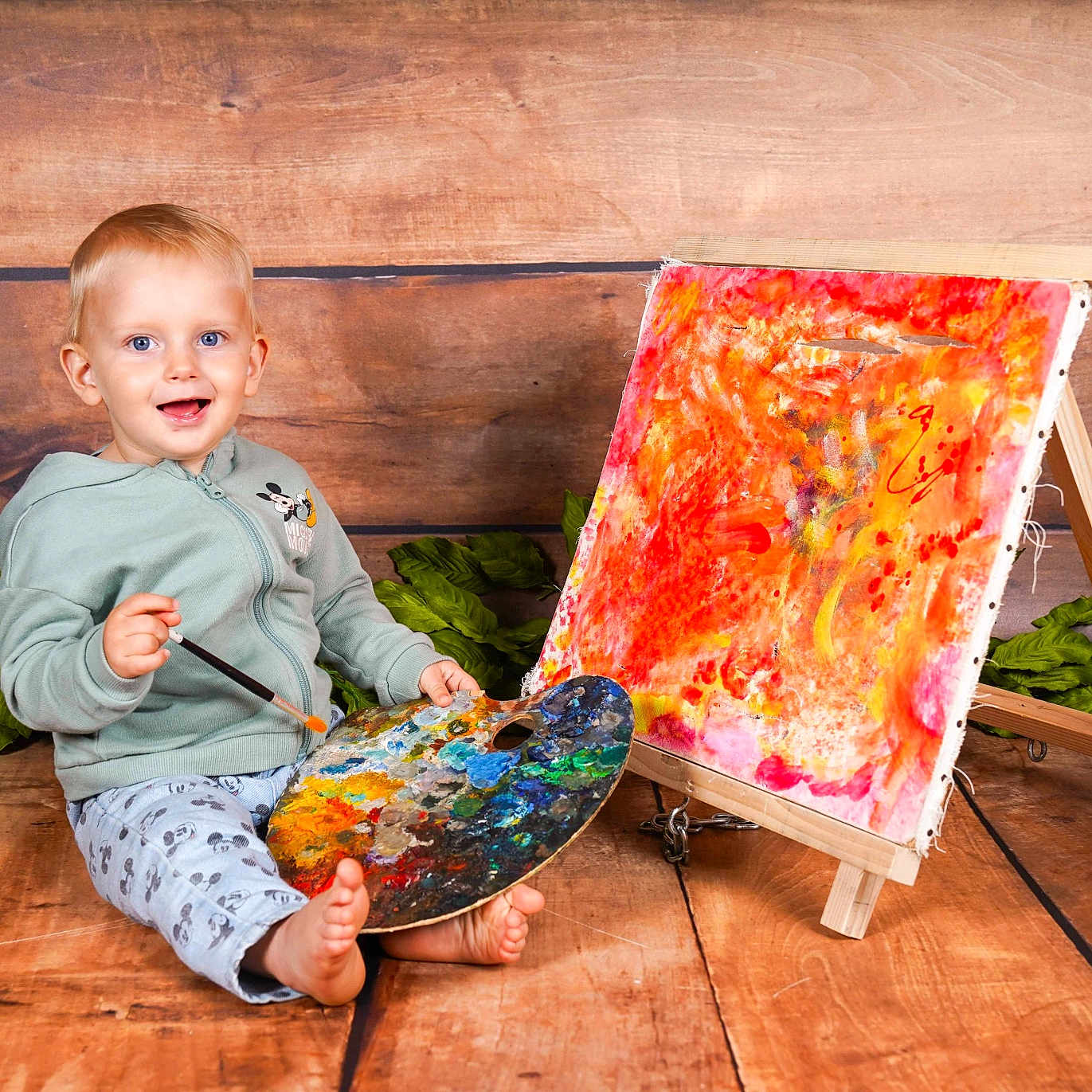 Kaysan participe au concours pour gagner de l'argent avec cette photo : artwork, barefoot, child, colorful, creative, easel, green_leaves, happy, hoodie, indoor, paintbrush, painting, palette, pants, portrait, sitting, smiling, toddler, wooden_background, wooden_floor