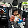child, car_seat, plush_toy, vehicle_interior, window, suburban, seatbelt, clothing, person, toy, hair, face, car, child_seat, sitting, safety, inside, daylight, expression, transportation