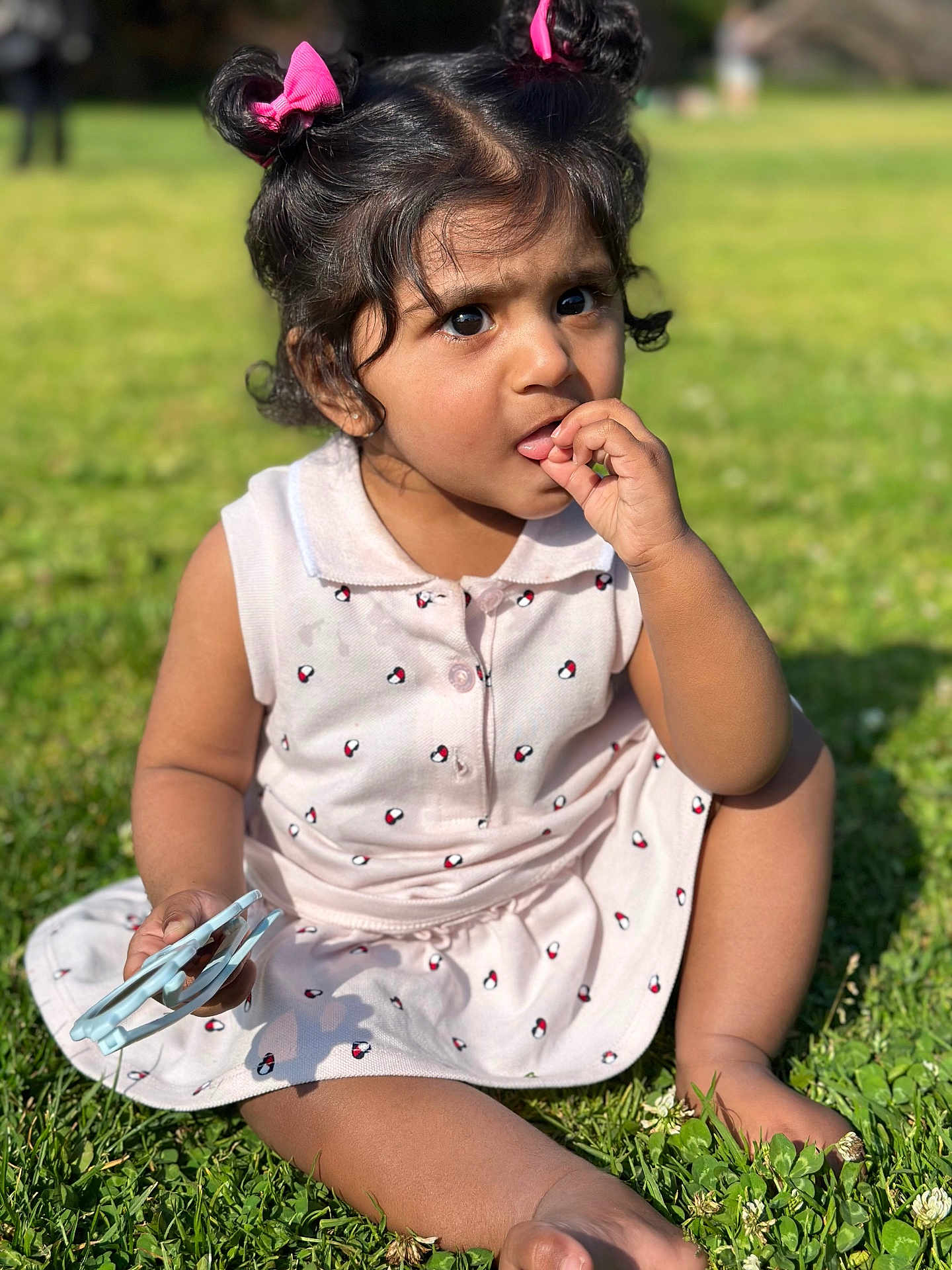 Ishika joined the competition — help win amazing prizes! child, toddler, girl, grass, outdoor, sunlight, dress, pink, hair_ties, curly_hair, barefoot, holding_object, sitting, nature, greenery, summer, cute, portrait, daylight, expression