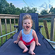 Layken joined the competition — help win amazing prizes! baby, child, smiling, happy, outdoor, lawn_chair, blue_sky, greenery, deck, wooden_railing, baby_clothes, tutu, sitting, face, person, summer, sunset, grass, fence, cute