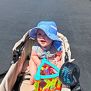 Layken joined the competition — help win amazing prizes! baby, blue_hat, bright_colors, casual_clothing, child, daytime, fan, happy, infant, outdoor, pavement, people, playful, smiling, stroller, summer, sun_protection, sunlight, toy, walking