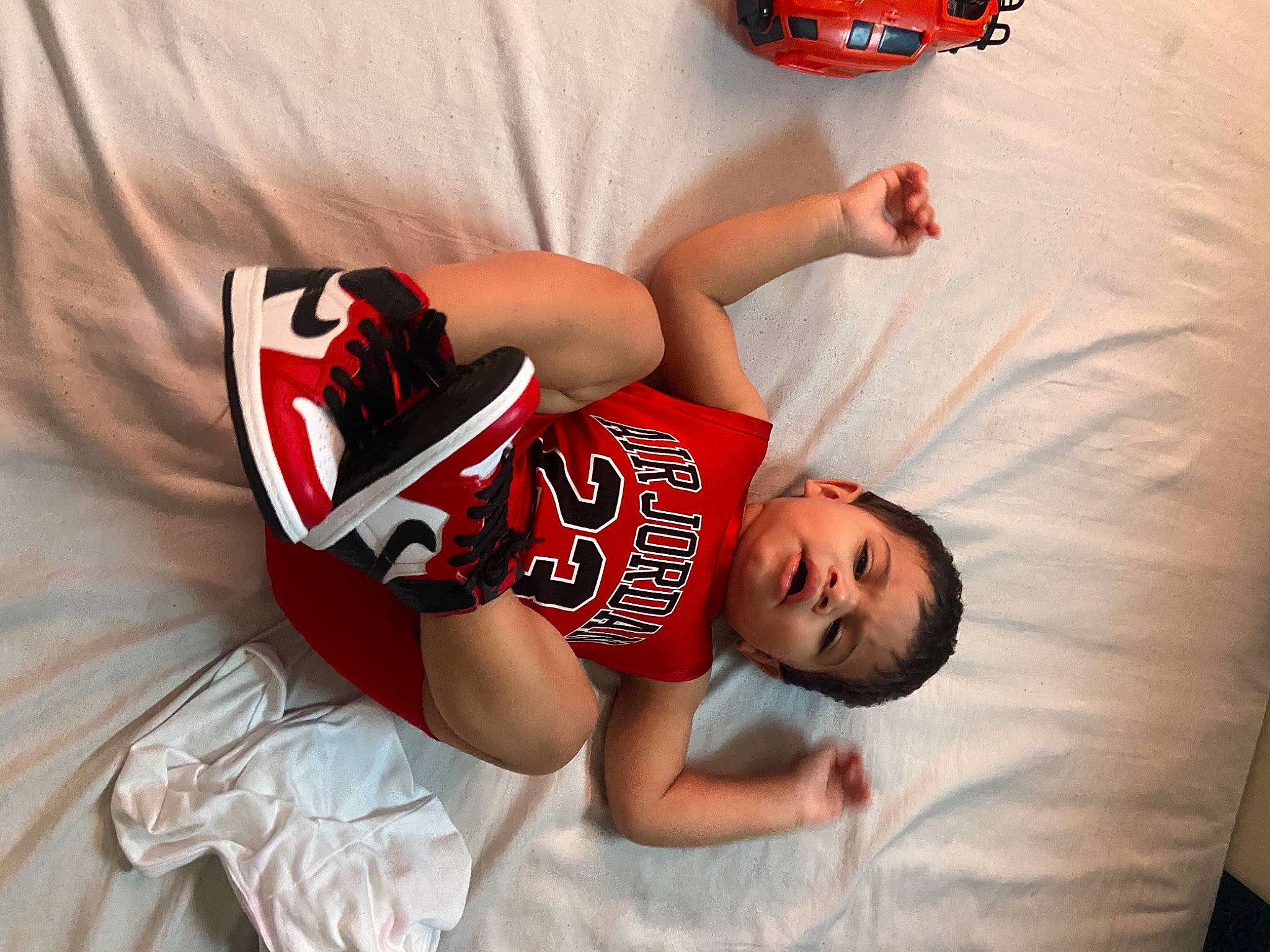 Isaiah is registered to the contest to win money with this photo: arm, baby_toddler_clothing, carmine, elbow, person, red, sports_jersey, toy, toy_vehicle, walking_shoe