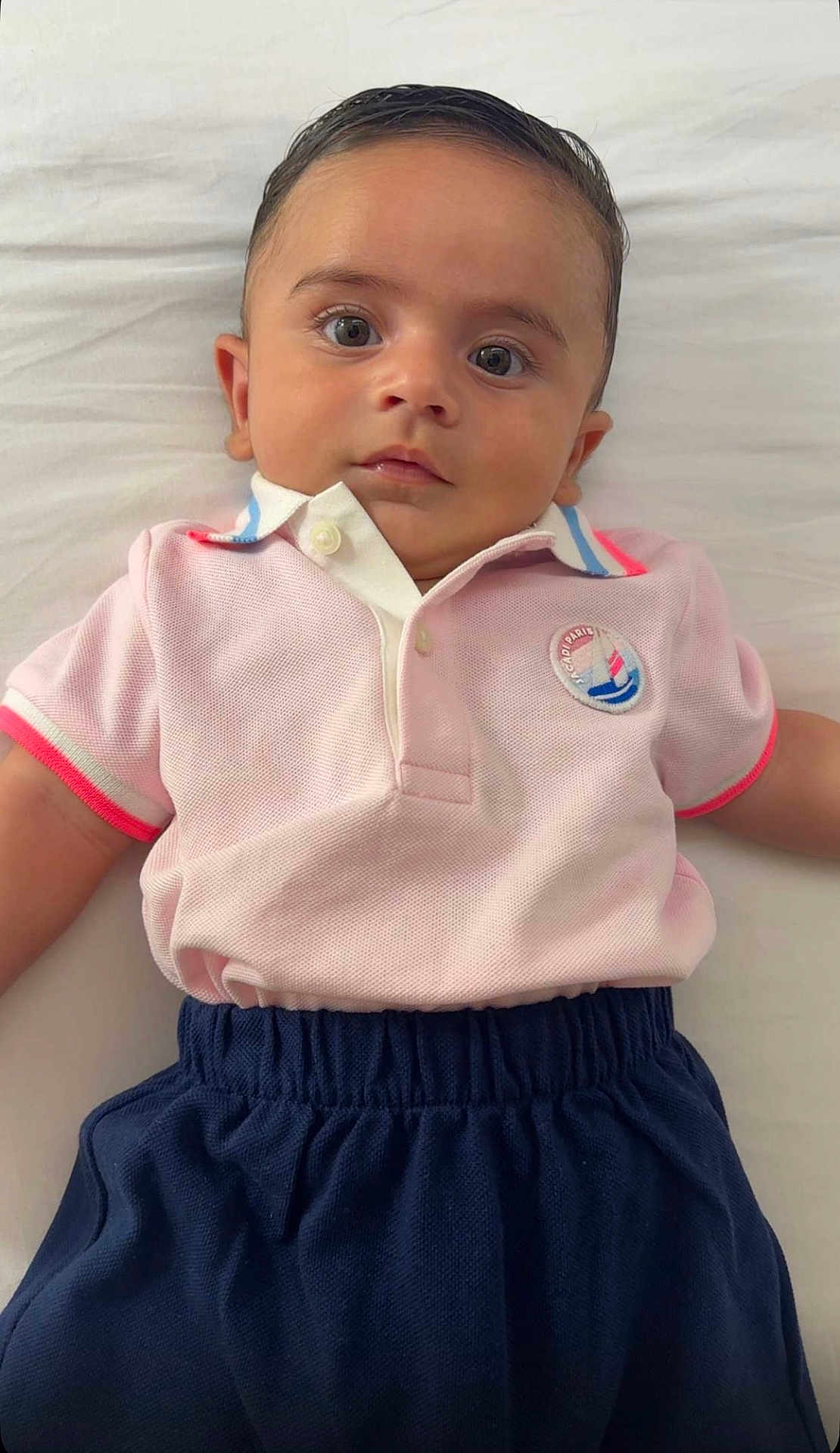 Fael a rejoint le concours — aidez-le/la à gagner de superbes lots ! baby, child, face, eyes, hair, pink_polo, navy_pants, clothing, infant, lying_down, white_background, portrait, cute, curious, indoors, young_child, skin, head, expression, casual_wear