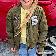 Lily Rose joined the competition — help win amazing prizes! child, girl, red_headband, blonde_hair, green_jacket, yellow_top, blue_jeans, white_shoes, fluffy_slippers, car, red_car, car_wheel, outdoor, sidewalk, smiling, portrait, casual_clothing, daylight, standing, happy