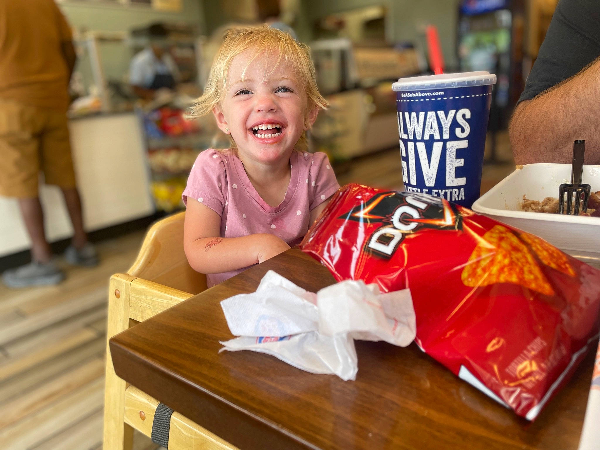 Maci is registered to the contest to win money with this photo: carbonated_soft_drinks, carmine, chair, child, cuisine, drink, event, flooring, food, happy, hardwood, joy, leisure, person, recreation, smile, t_shirt, table, toddler, varnish