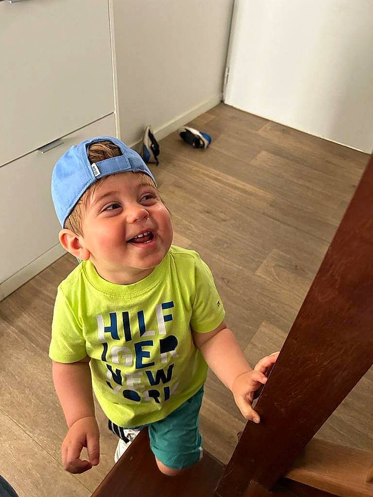 Ishaq a rejoint le concours — aidez-le/la à gagner de superbes lots ! baby_toddler_clothing, baseball_cap, cap, child, cricket_cap, floor, flooring, fun, happy, hardwood, hat, headwear, person, shorts, sleeve, smile, standing, t_shirt, toddler, varnish