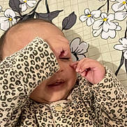 Rania is registered to the contest to win money with this photo: baby, child, infant, leopard_print, clothing, hand, face, sleepwear, cute, playing, patterned, floral, background, lying_down, skin, young, adorable, cozy, indoors, expression