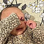 baby, child, infant, leopard_print, clothing, hand, face, sleepwear, cute, playing, patterned, floral, background, lying_down, skin, young, adorable, cozy, indoors, expression