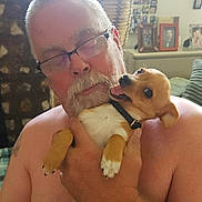 Peanut joined the competition — help win amazing prizes! man, dog, glasses, shirtless, indoor, holding, pet, happy, small_dog, beard, tattoo, plant, photo_frames, couch, furniture, close_up, portrait, smiling_dog, home, cozy