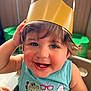 toddler, child, smiling, crown, paper_crown, tank_top, cartoon, popsicle, high_chair, indoor, happy, cute, short_hair, blue_shirt, teeth, face, person, sitting, playful, bright