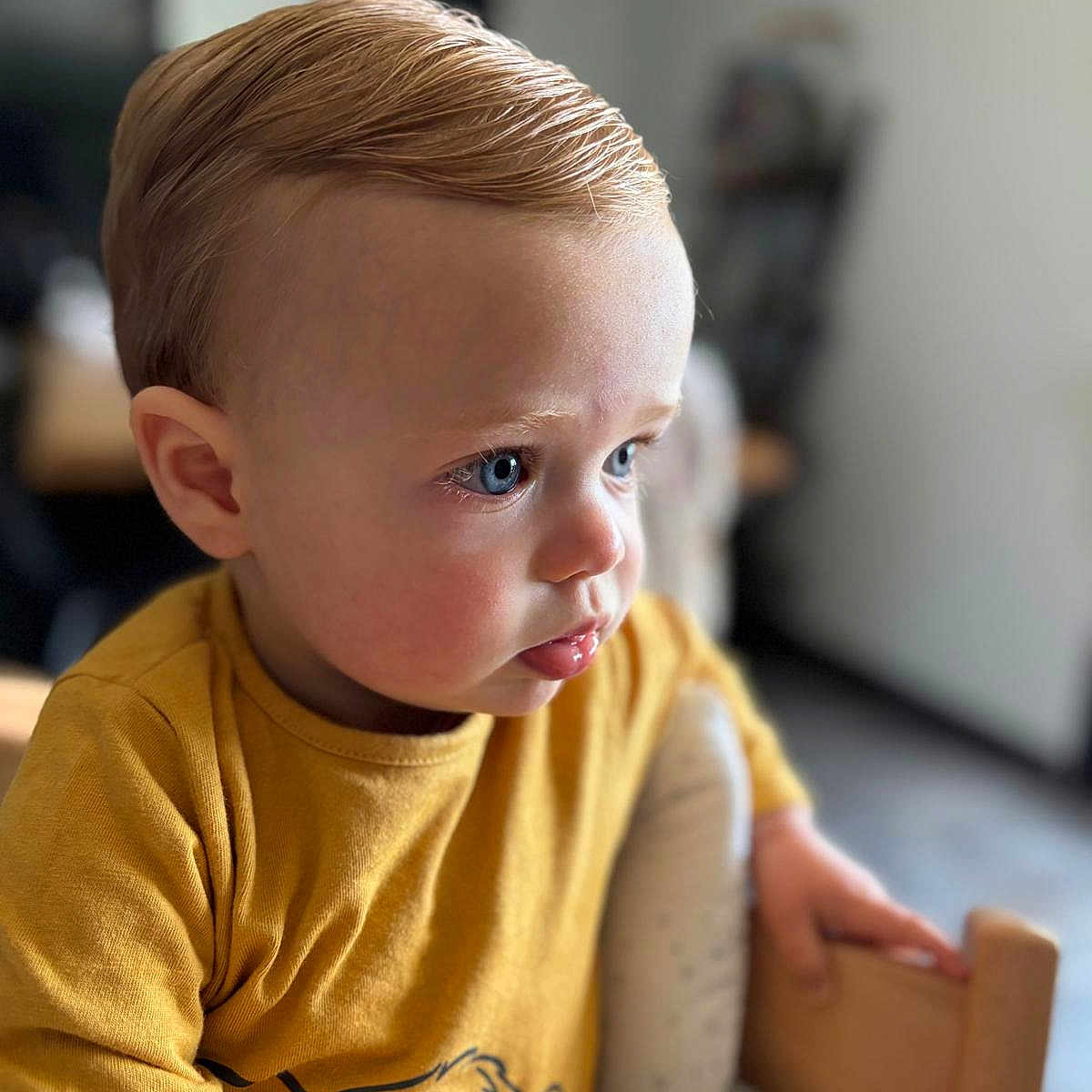 Zayonn a rejoint le concours — aidez-le/la à gagner de superbes lots ! baby, blond_hair, blue_eyes, cartoon_lion, casual_clothing, child, close_up, curious, cute, expression, focused, high_chair, home, indoor, mustard_shirt, portrait, seated, soft_light, toddler, young_child