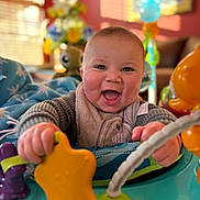 Nickeil is registered to the contest to win money with this photo: baby, smiling, toy, star_shaped_toy, activity_center, indoor, child, happy, hands, face, playtime, colorful, cozy, living_room, blurred_background, cheeks, sweater, blanket, infant, cute