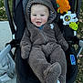 baby, child, stroller, onesie, bear_ears, toy, outdoor, smile, happy, infant, clothing, blanket, person, cute, seat, plush, hood, face, grass, sidewalk