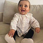 Elya participe au concours pour gagner de l'argent avec cette photo : baby, black_leggings, child, couch, cozy, cute, expression, face, footwear, furniture, hand, happy, human, indoors, portrait, sitting, skin, smiling, white_blouse, young_child