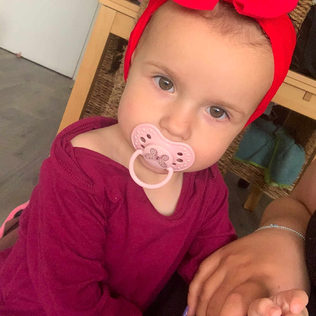 Ruby a rejoint le concours — aidez-le/la à gagner de superbes lots ! child, curious_expression, eyes, face, floor, furniture, hair, hand, headband, holding_hands, indoor, nail_polish, pacifier, person, purple_clothing, red_bow, skin, toddler, wicker_chair, wooden_table