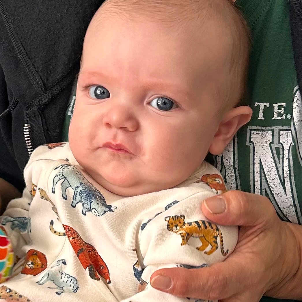 Lucas is registered to the contest to win money with this photo: adult, animal_print, baby, blue_eyes, casual, closeup, clothing, cute, expression, face, hand, head, holding, indoor, infant, onesie, person, portrait, skin, young_child