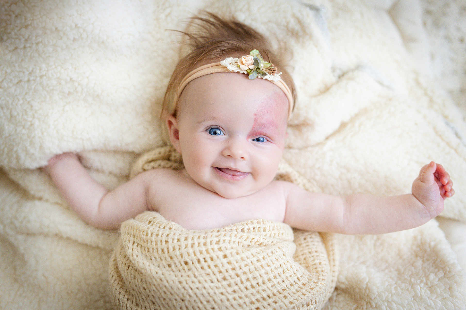 Lia participe au concours pour gagner de l'argent avec cette photo : baby, smiling, headband, flower, blanket, blue_eyes, infant, cute, soft_texture, cozy, lying_down, happy, skin, hand, portrait, child, warm, indoors, fluffy, closeup