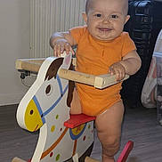 Lola participe au concours pour gagner de l'argent avec cette photo : baby, child, rocking_horse, toy, indoor, floor, wood, orange_clothing, smile, drool, furniture, window, radiator, play, happy, person, cute, infant, legs, hand