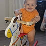 baby, child, cute, drool, floor, furniture, hand, happy, indoor, infant, legs, orange_clothing, person, play, radiator, rocking_horse, smile, toy, window, wood